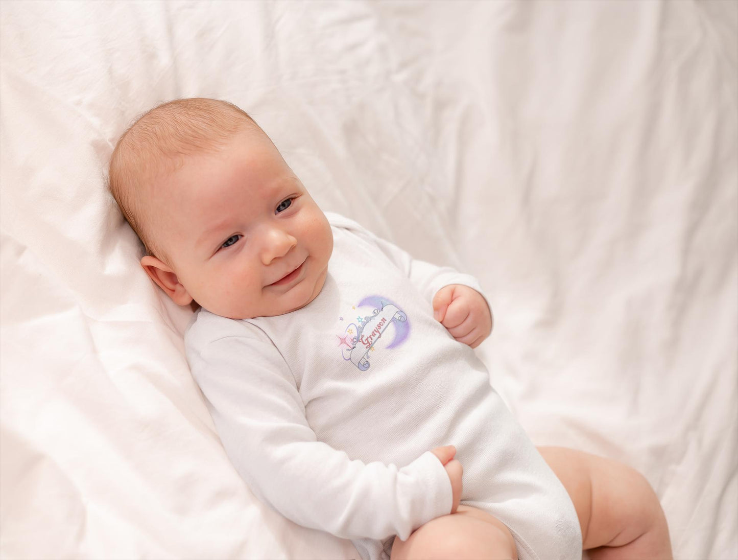 Baby wearing a white onesie with a colorful design on a white blanket