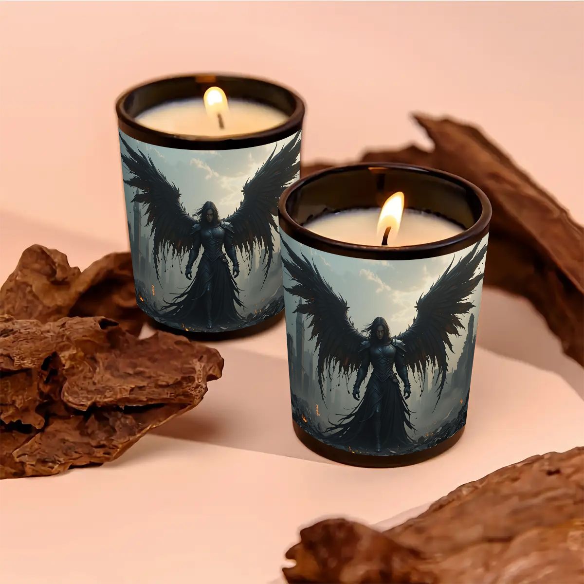Two lit candles in decorative holders with angel wings design on a soft pink background.