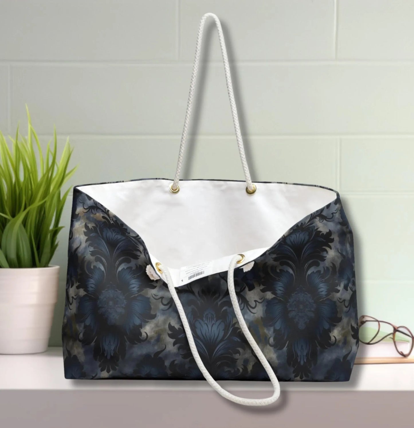 Tote bag with floral pattern on a white surface with a plant and glasses in the background