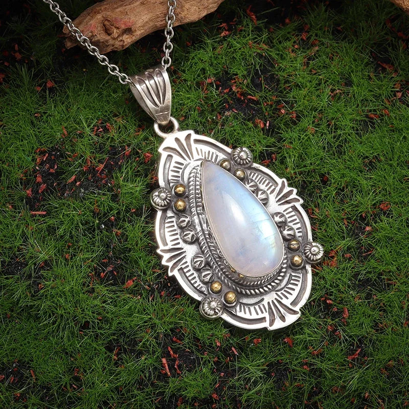 Silver pendant with a teardrop-shaped gemstone on a chain, placed on green moss.