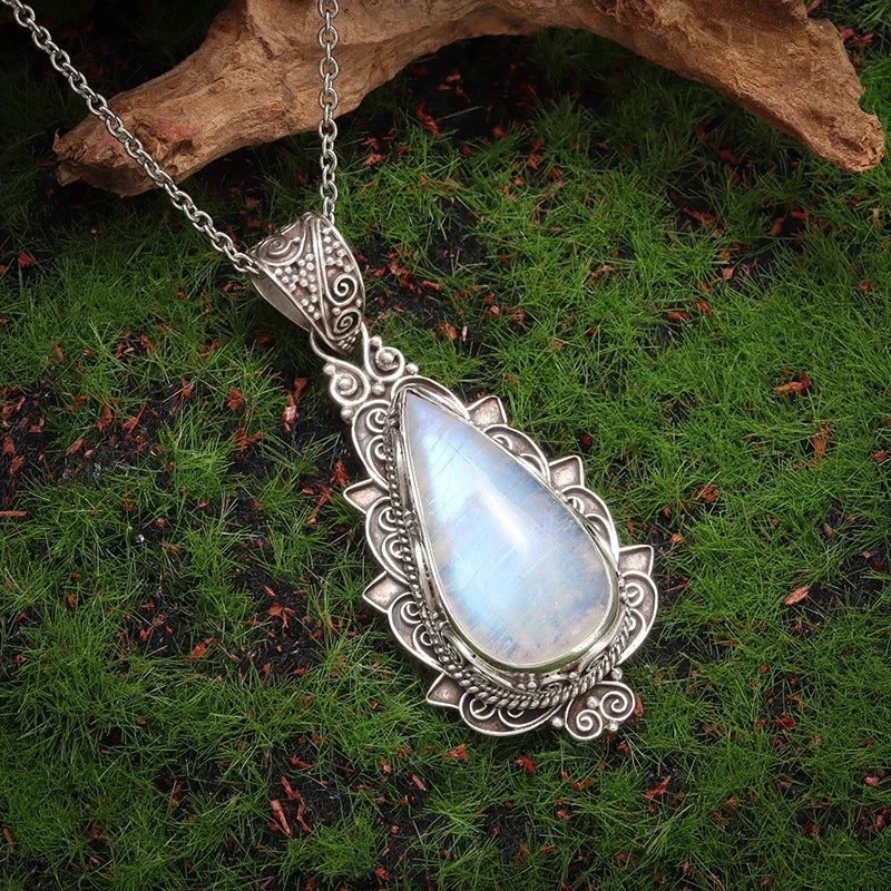 Silver pendant with a teardrop-shaped gemstone on a chain, placed on green grass.