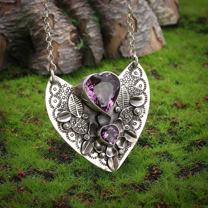 Silver pendant with purple heart-shaped stones on a grassy background
