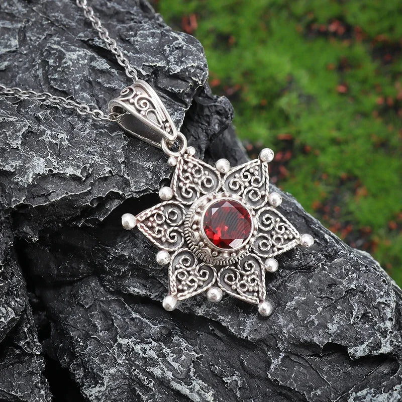 Silver pendant with a red gemstone on a dark rock with a green background