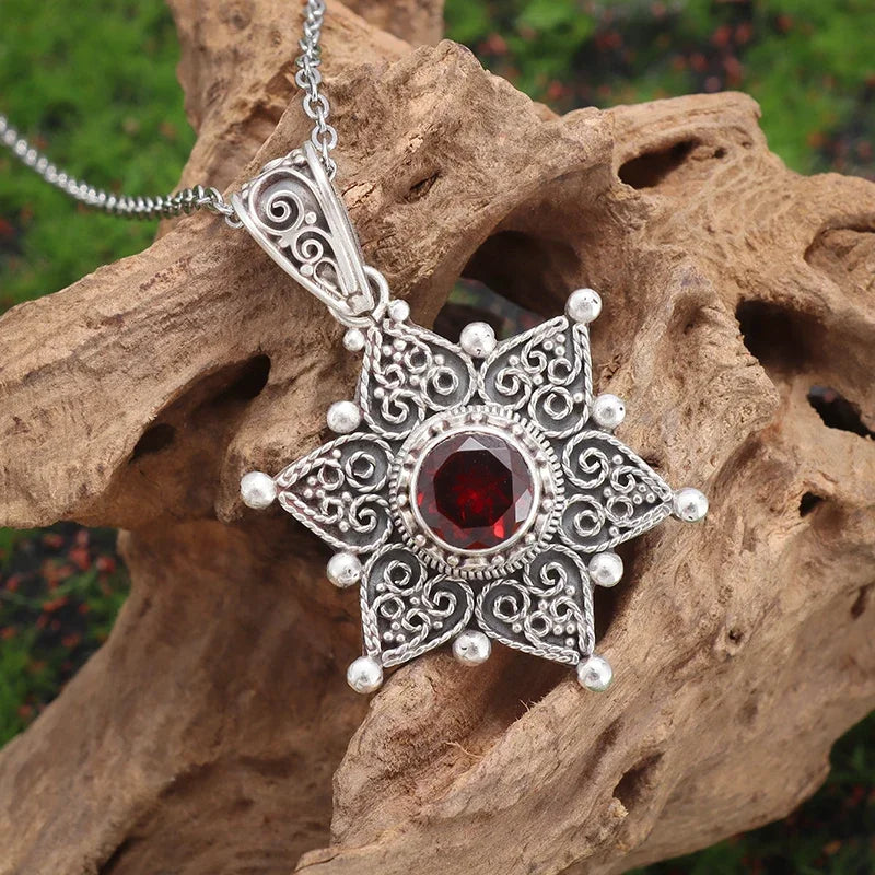 Silver pendant with a red gemstone on a wooden surface
