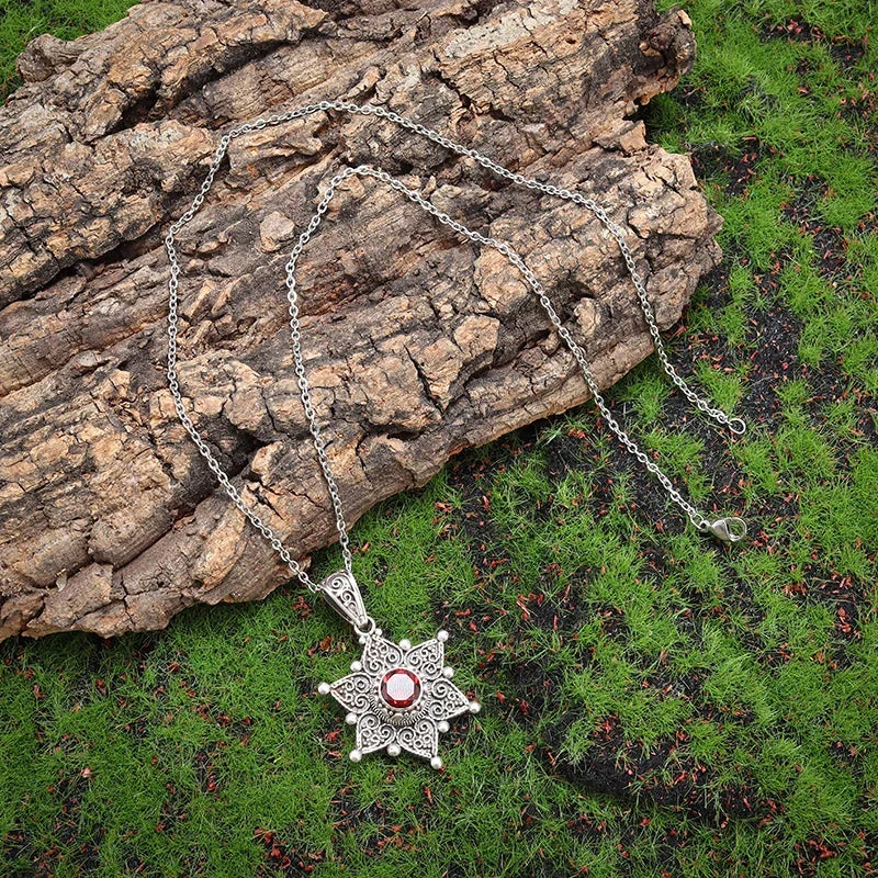 Silver necklace with a star-shaped pendant on a wooden log and grass background