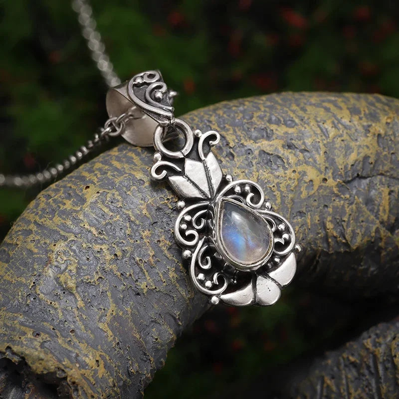 Silver pendant with a teardrop-shaped gemstone on a rock
