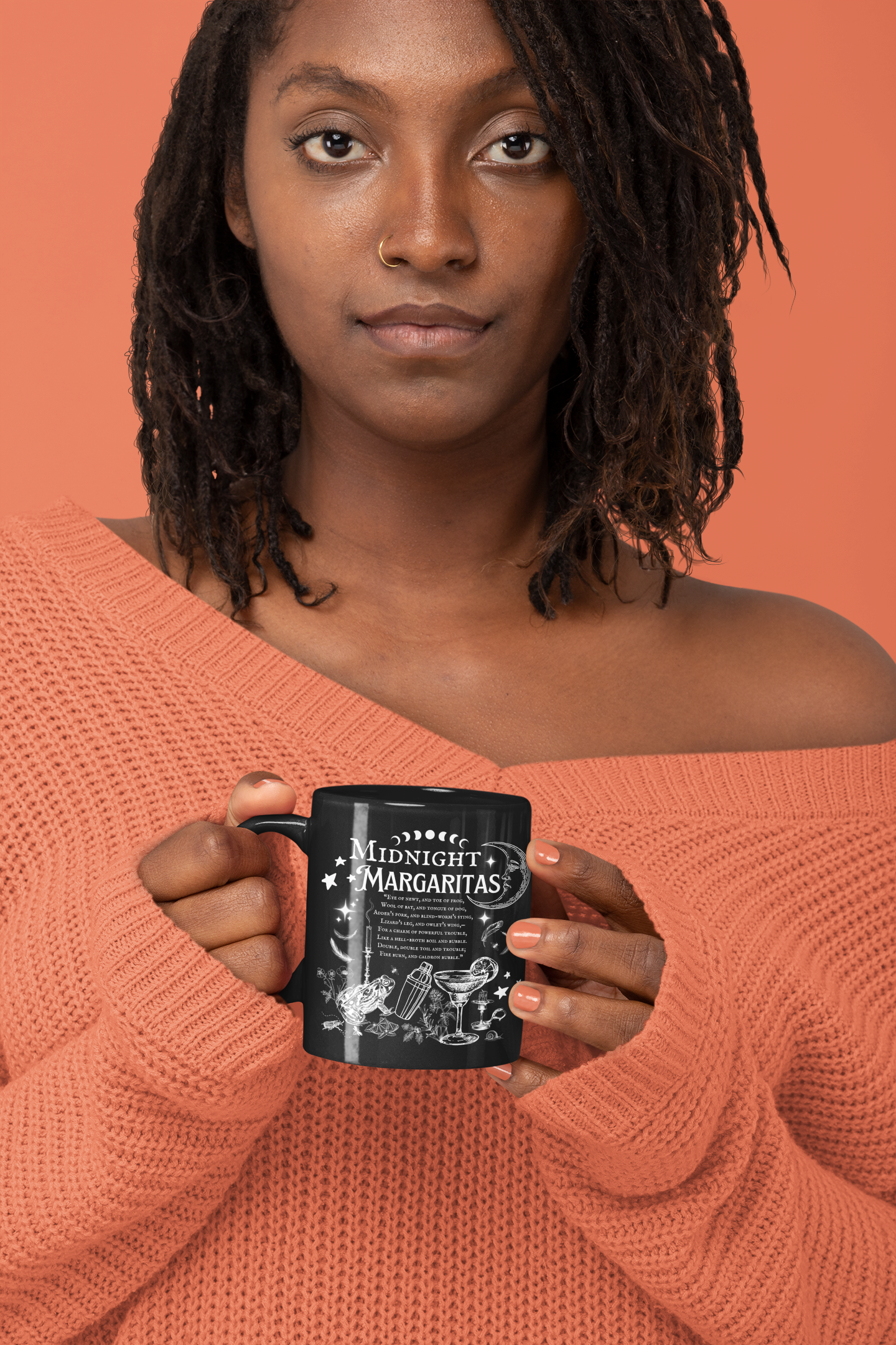 Person wearing an orange sweater holding a black mug with text against an orange background