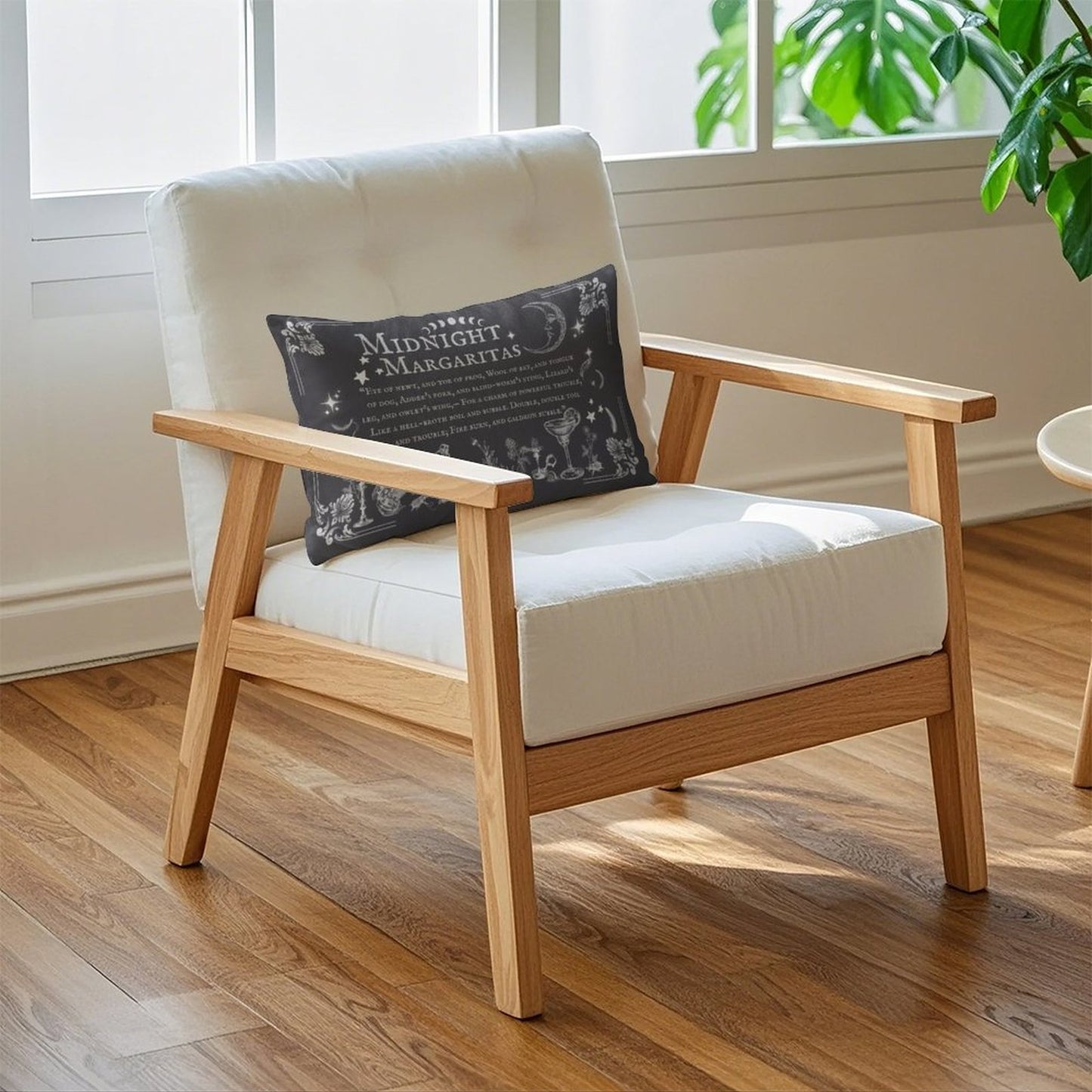 Wooden armchair with white cushion and dark pillow in a room with large windows and plants.