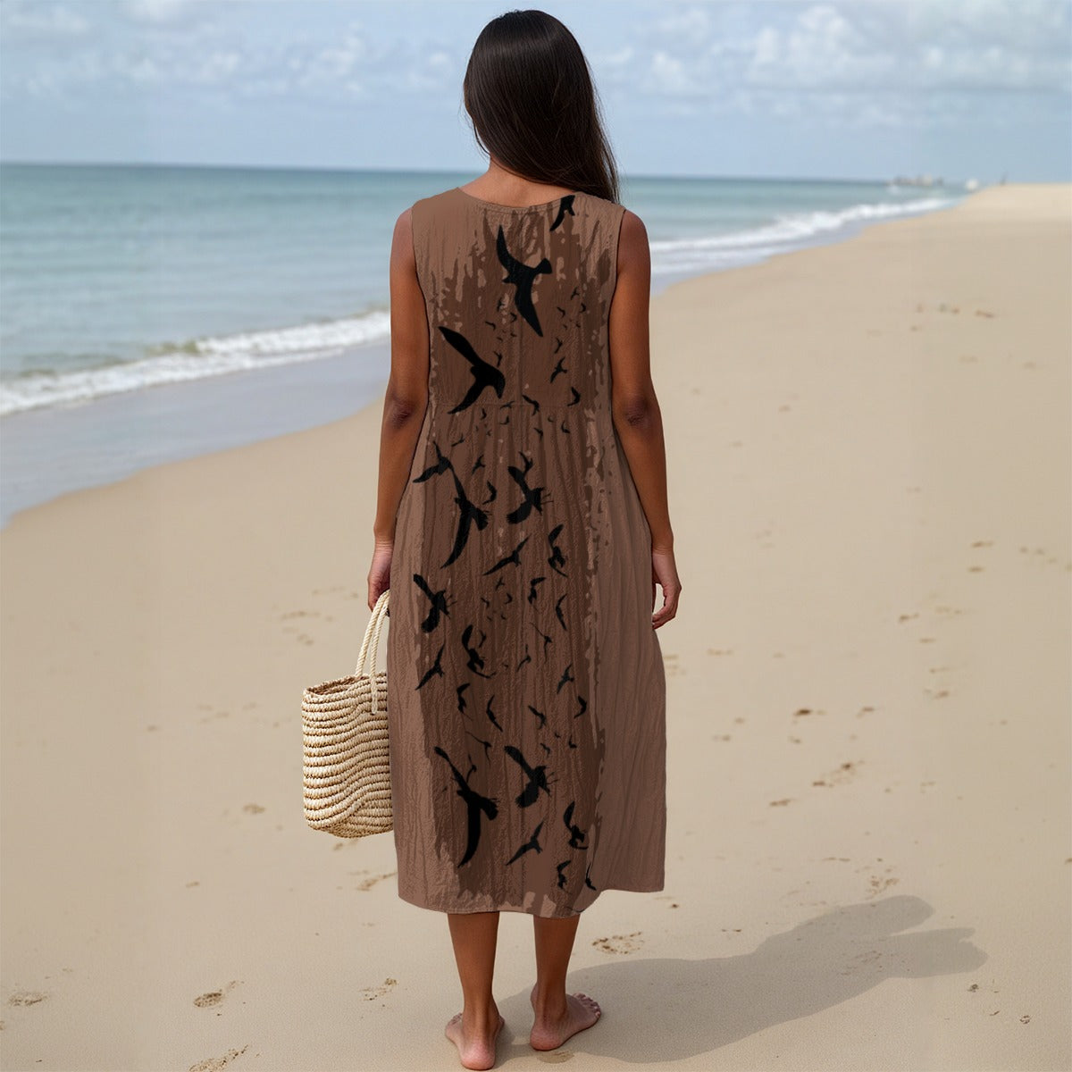 Woman in a brown dress with black bird patterns standing on a sandy beach.
