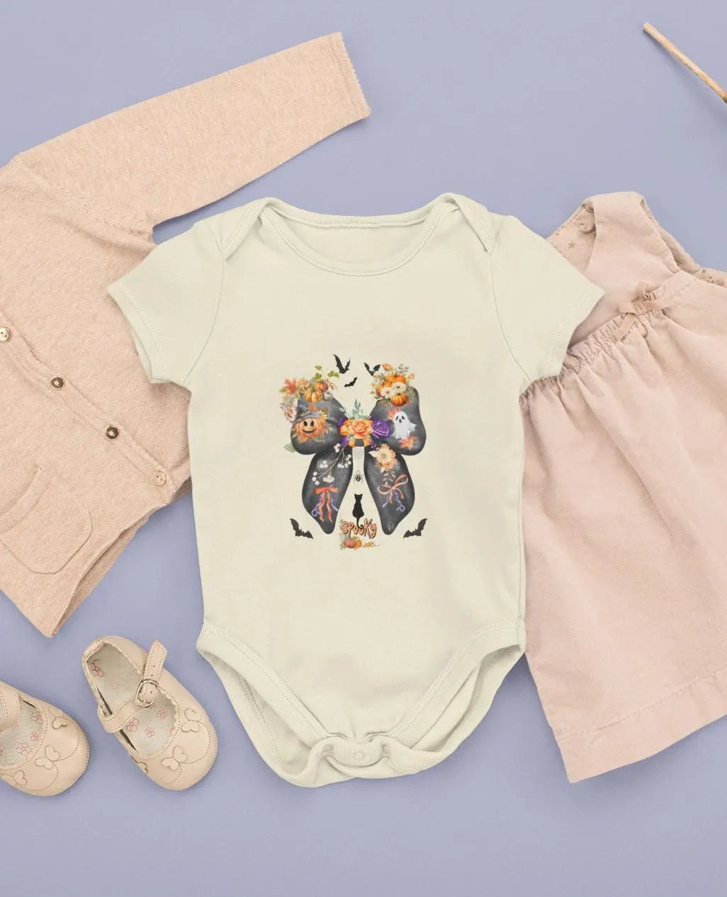 Baby outfit with floral bow design on a light yellow onesie, surrounded by pink pants, shoes, and a beige cardigan on a purple background.