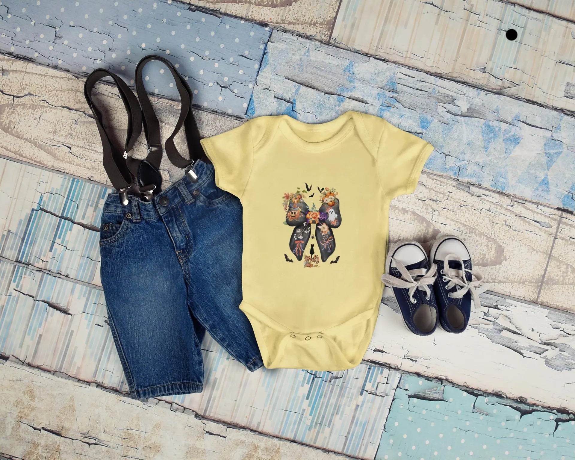 Baby outfit with yellow onesie, blue jeans, and shoes on a wooden surface