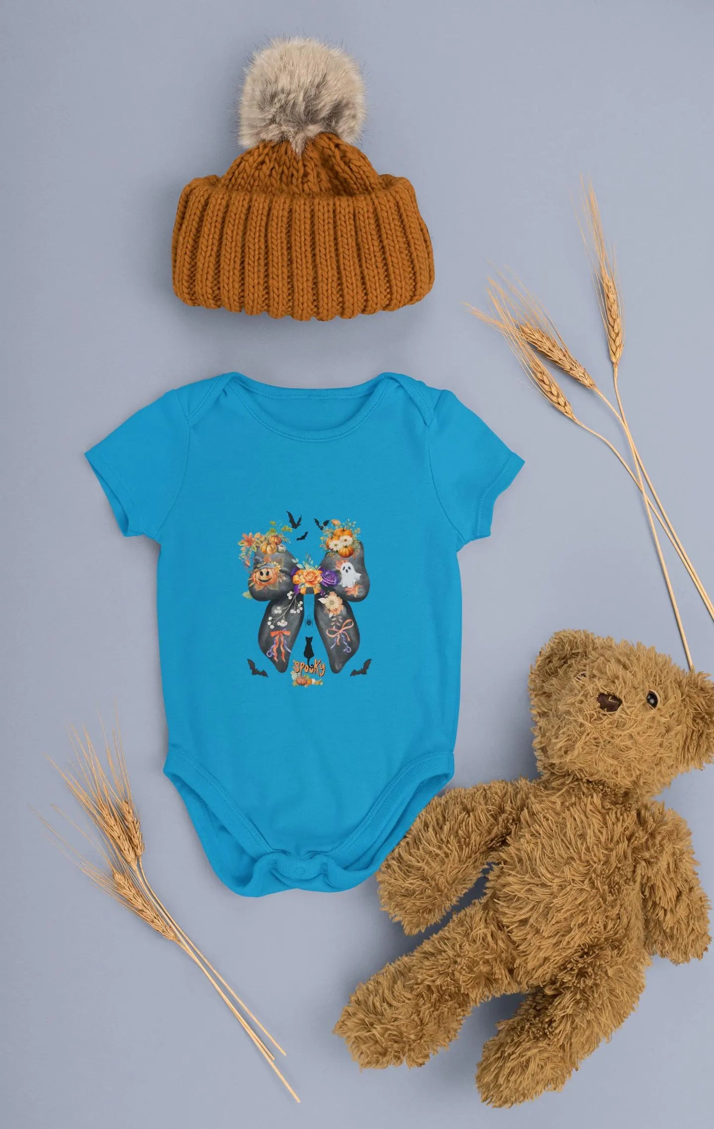 Blue baby onesie with a butterfly design, brown knit hat, and teddy bear on a gray background.