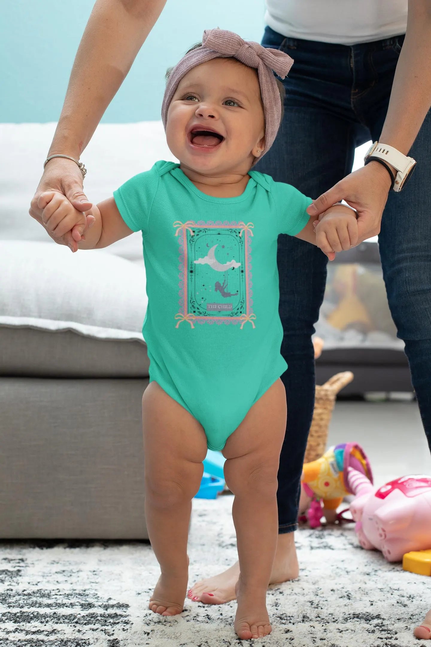 Baby in a green onesie with a whale design, standing on a carpeted floor.