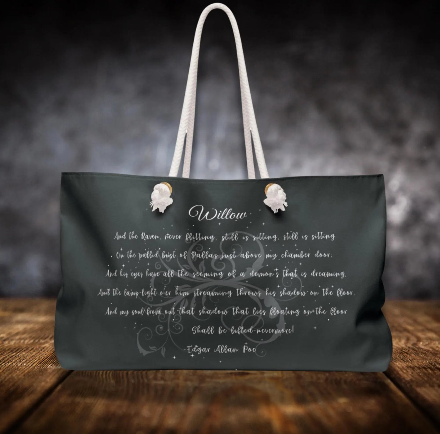 Black tote bag with white text and floral designs on a wooden surface