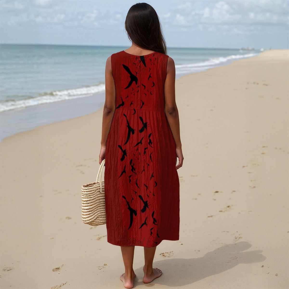 Woman in a red dress with black bird patterns standing on a beach.