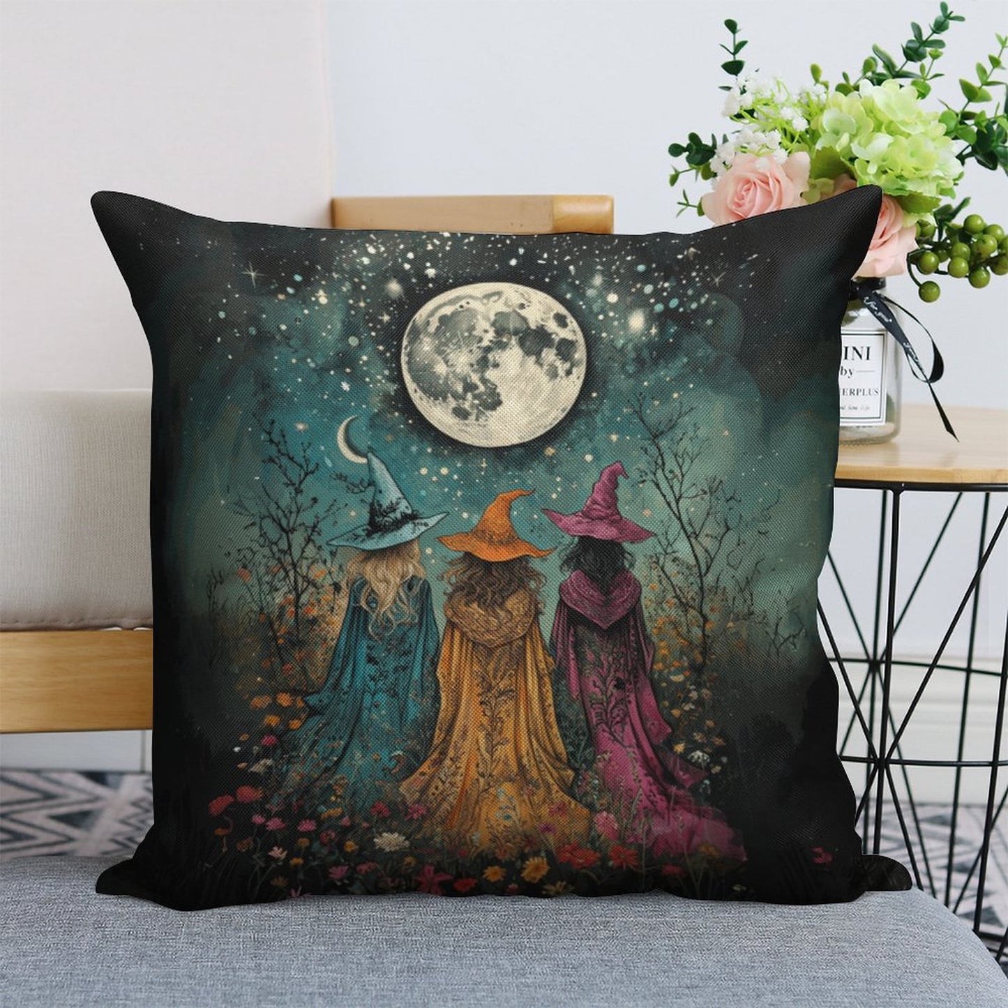 Decorative pillow with three witches under a moonlit sky on a couch.