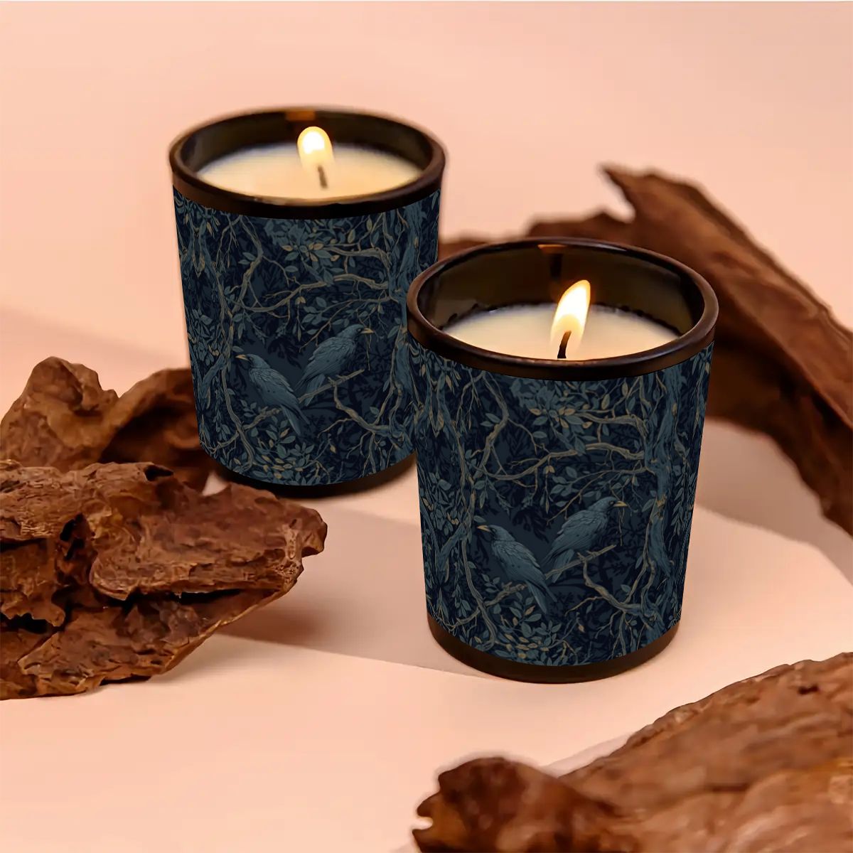 Two lit candles in blue patterned holders surrounded by natural elements on a pink background