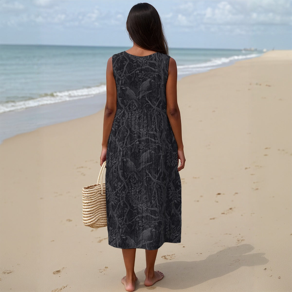 Woman in a black patterned dress standing on a beach with ocean view