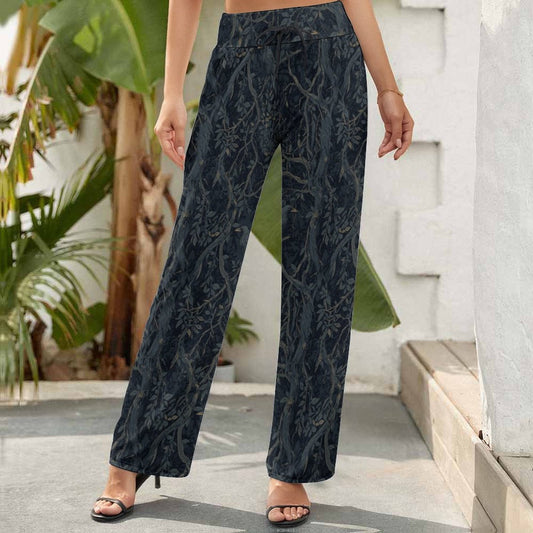 Person wearing dark floral-patterned pants standing outdoors with plants and a building in the background.