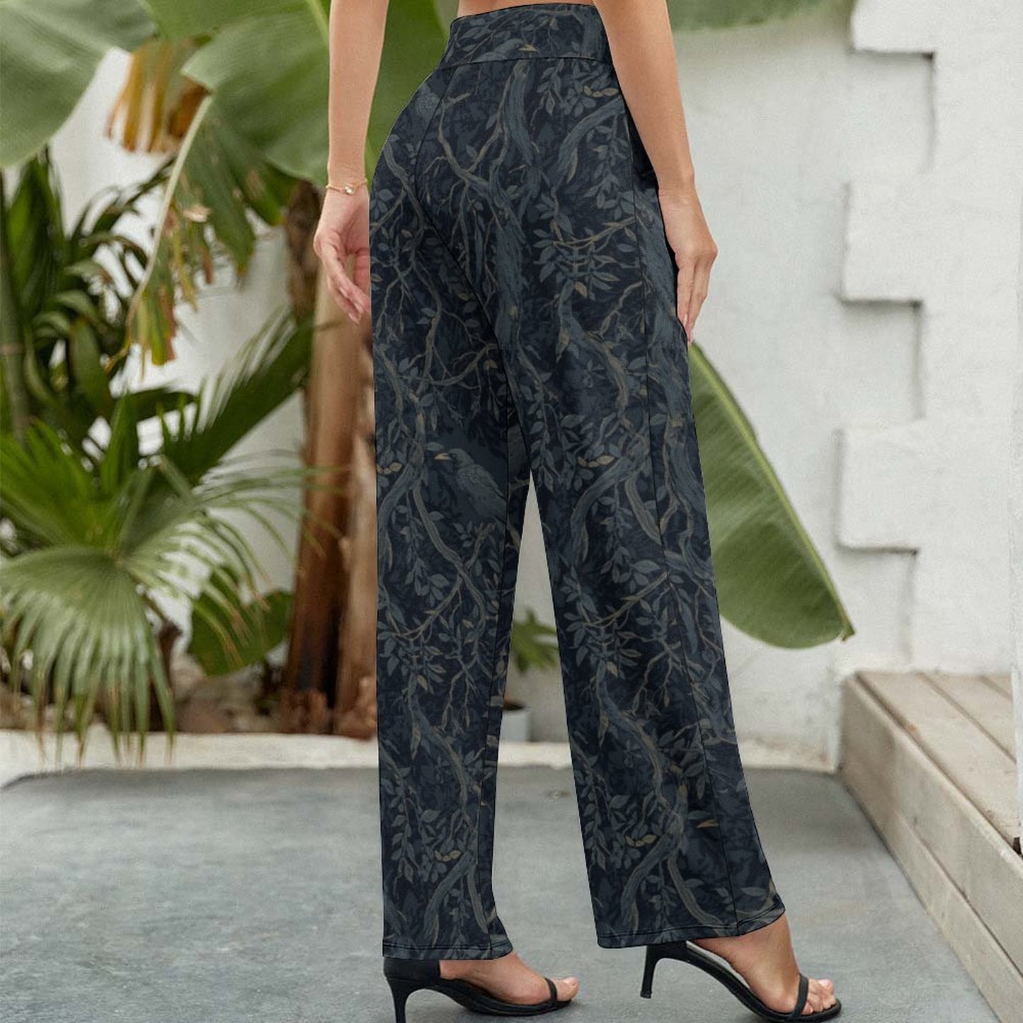 Person wearing dark patterned pants standing outdoors with plants in the background