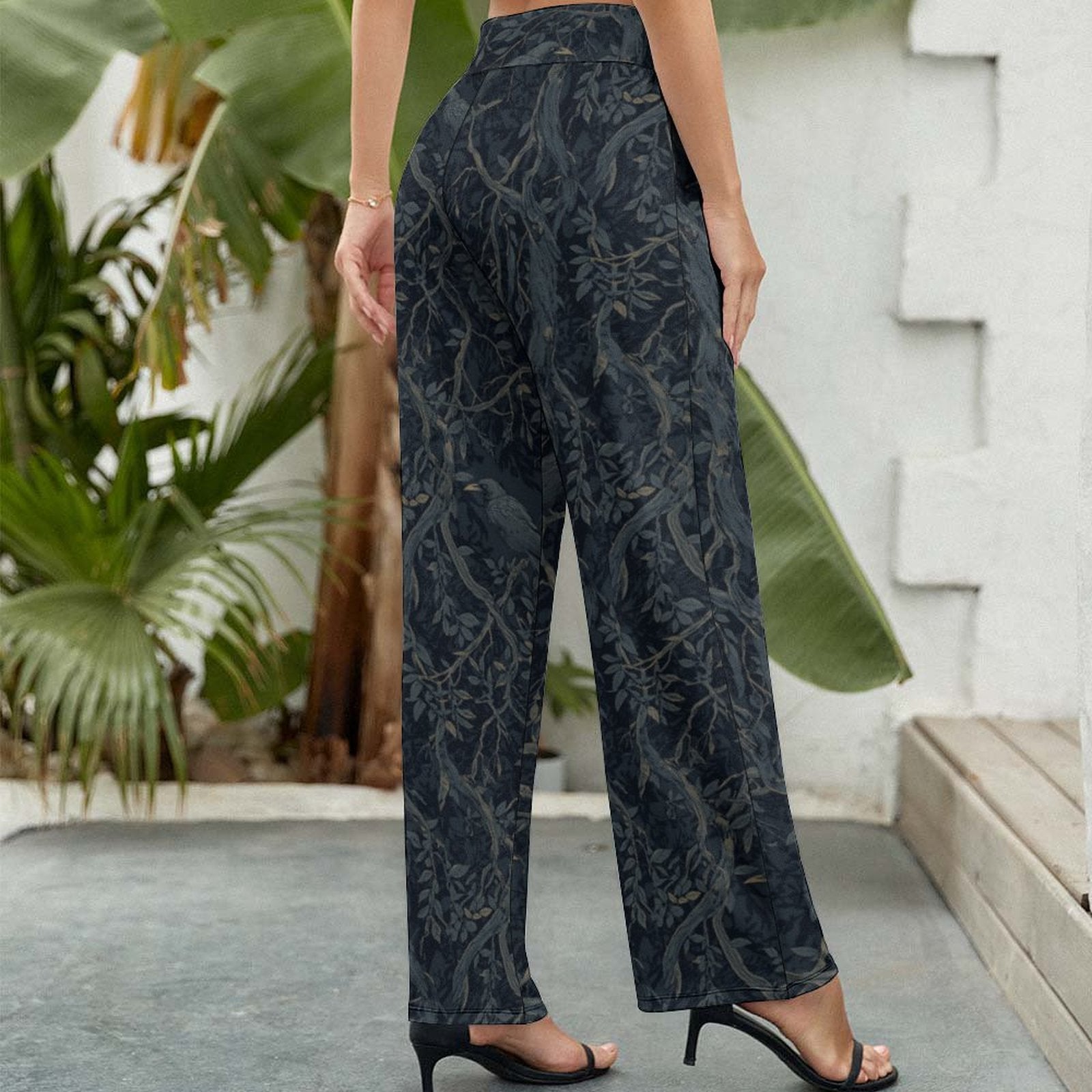 Person wearing dark patterned pants standing outdoors with plants in the background