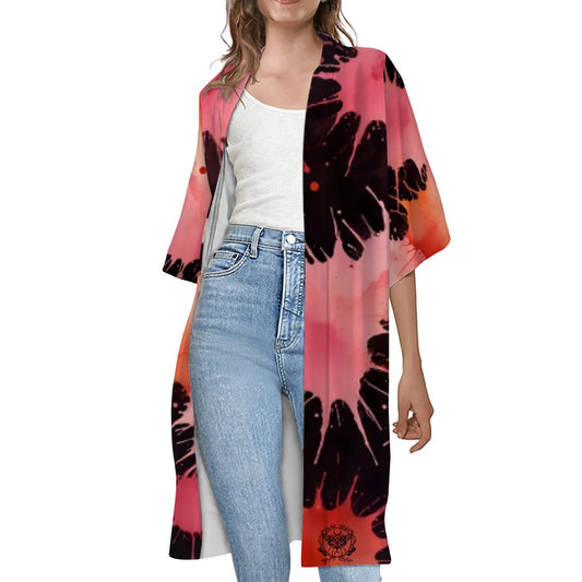 A woman wearing a short sleeve cape with a multicolored floral design over a white top and blue jeans.