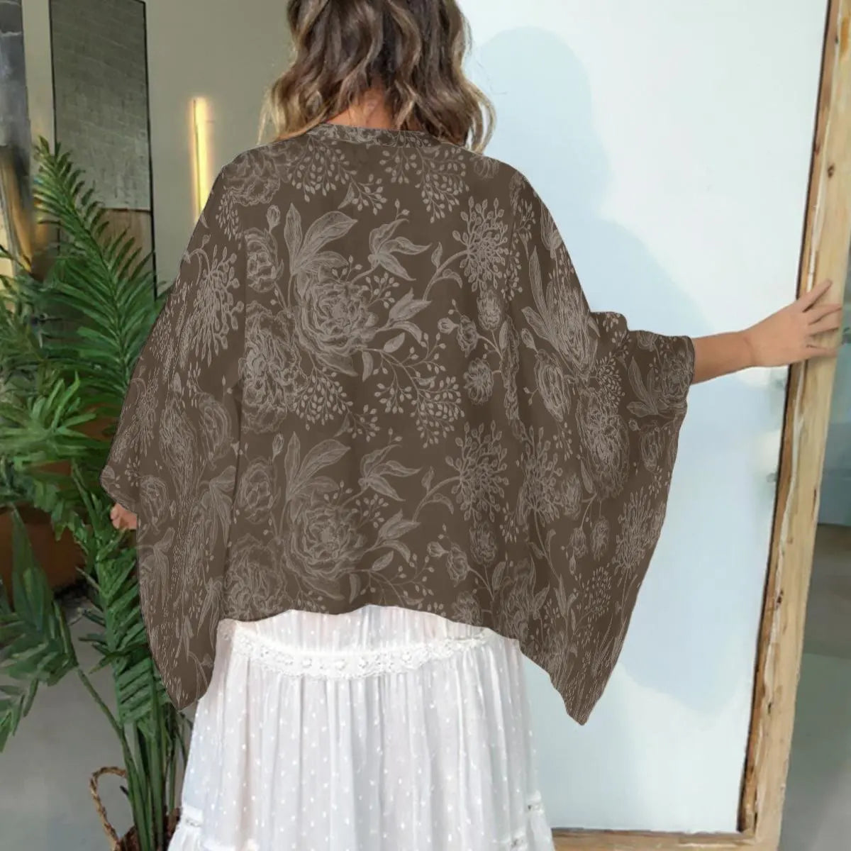 Woman wearing a brown floral patterned kimono over a white dress, standing in front of a mirror.