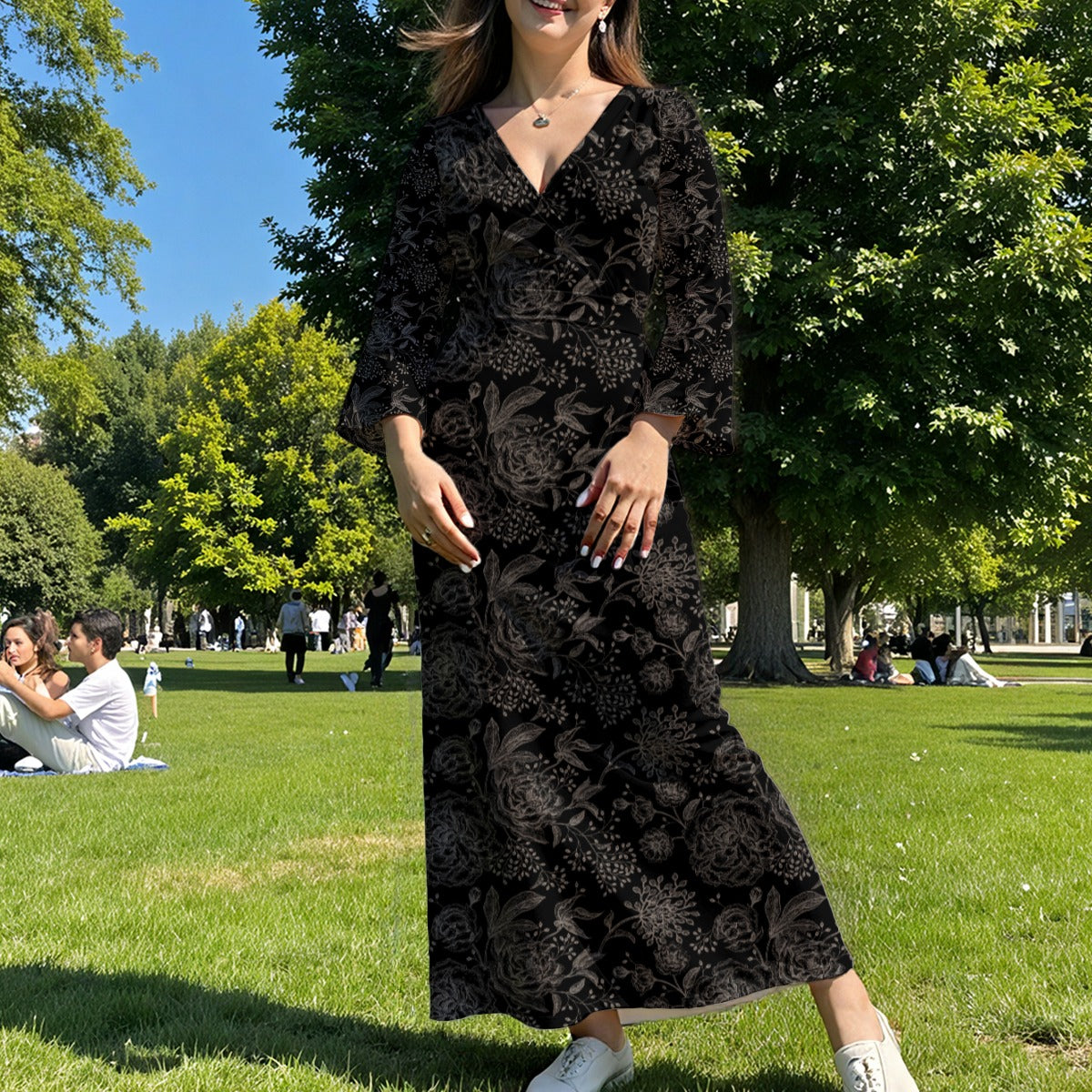 Woman in a black floral dress standing in a park with green grass and trees.