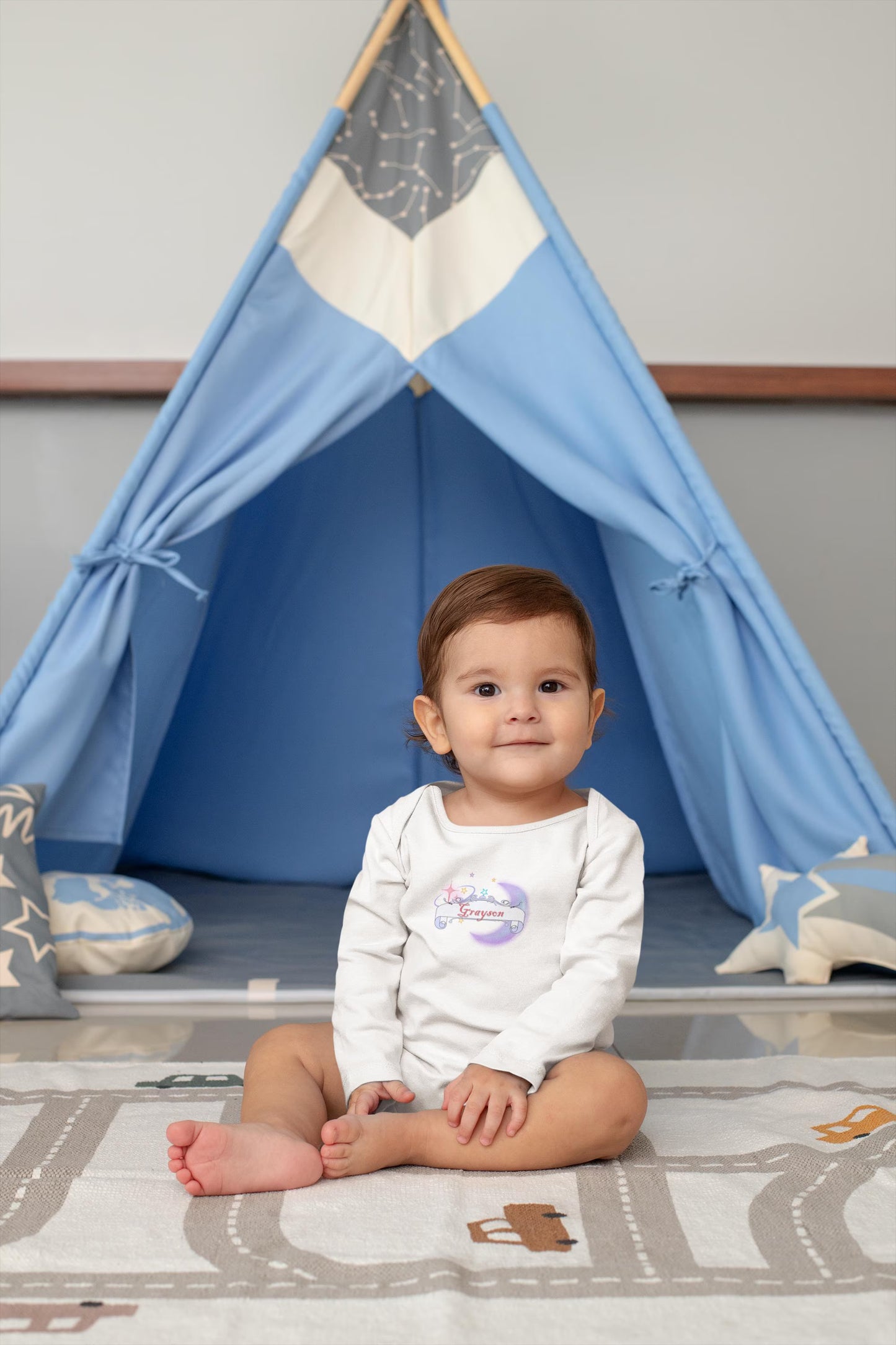 Baby sitting on the floor in front of a blue teepee