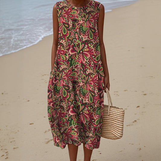 Woman in a colorful floral dress holding a straw bag on a beach.