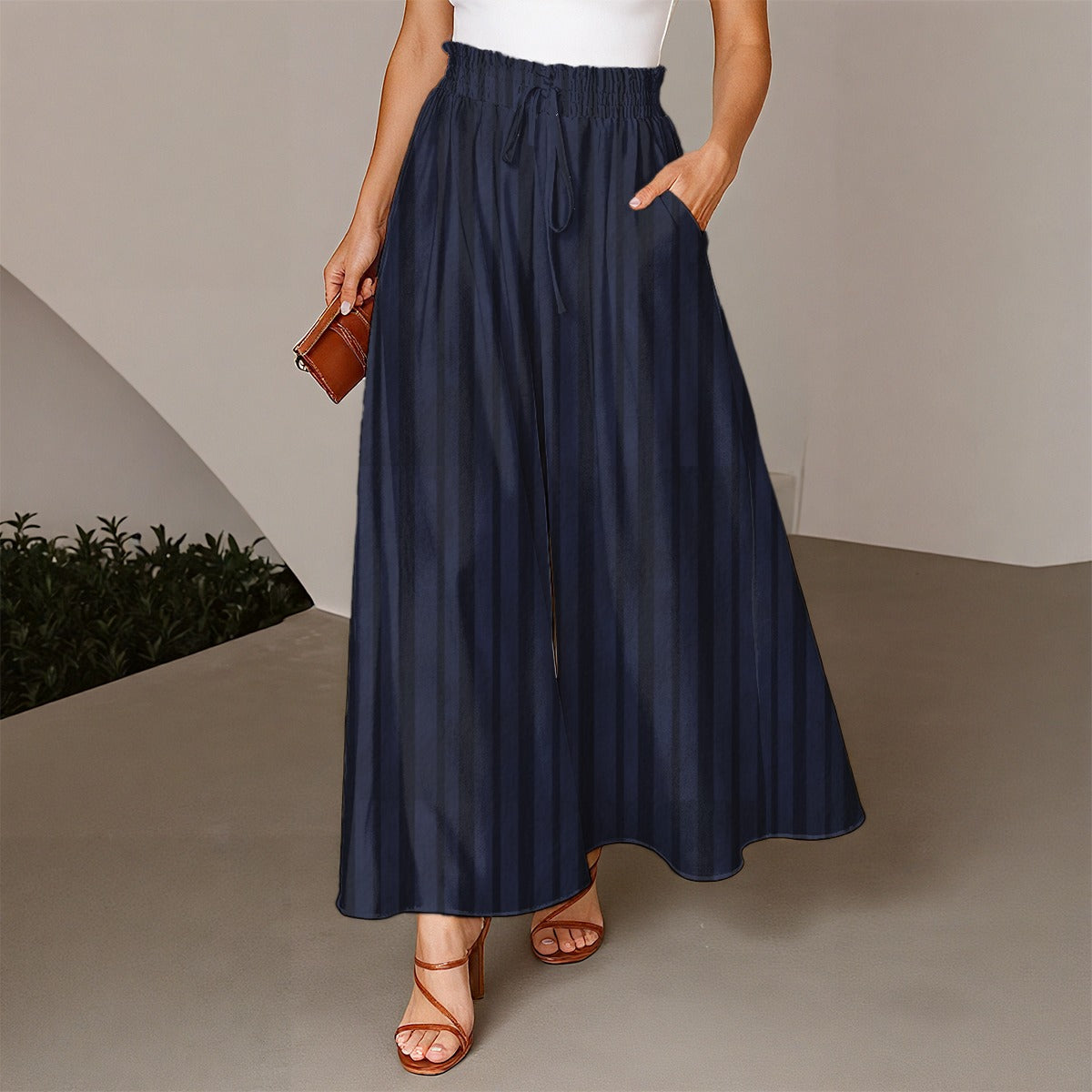 Person wearing a navy blue skirt with a white top and brown sandals on a neutral background