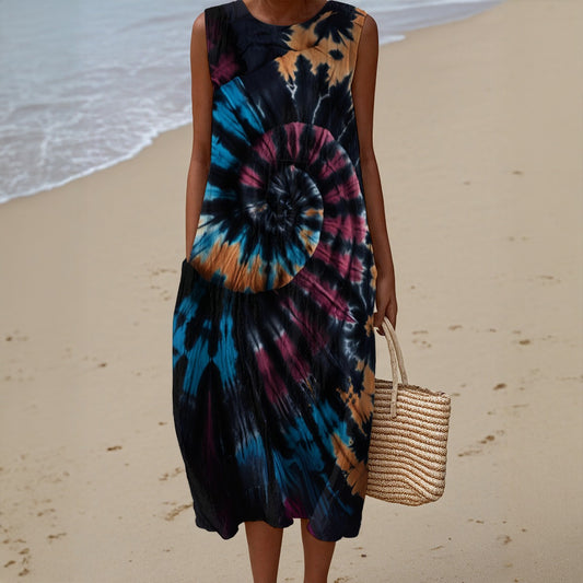 Person wearing a tie-dye dress on a beach holding a woven bag.