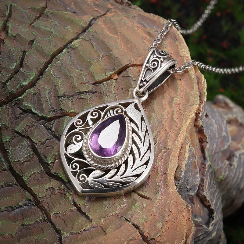 Silver pendant with purple gemstone on a wooden surface