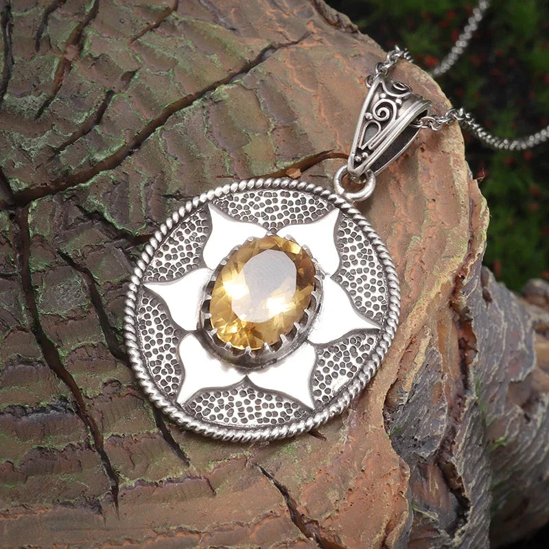 Silver pendant with a yellow gemstone on a textured stone surface