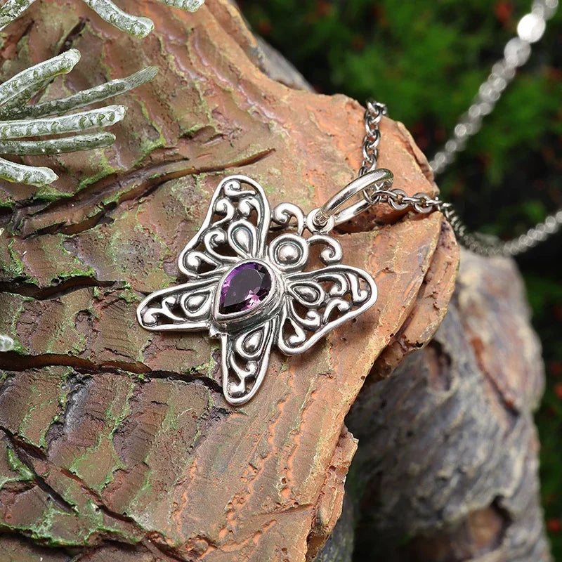 Silver butterfly pendant with purple gemstone on a chain, resting on textured wood.