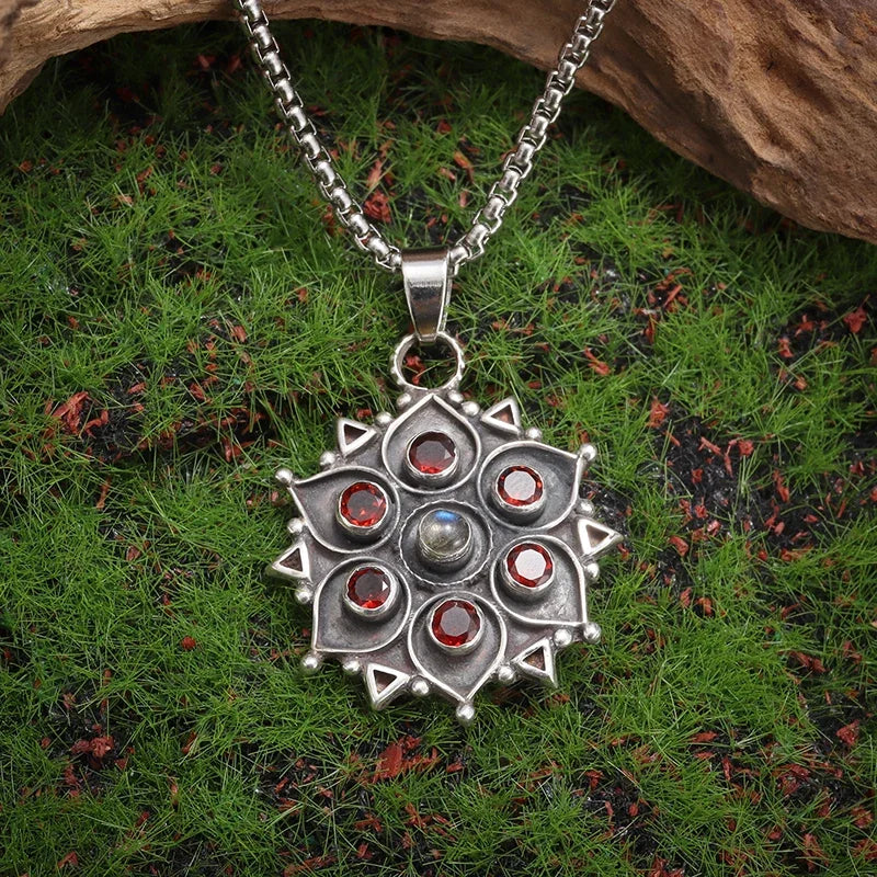 Silver pendant with red stones on a chain, placed on green grass.