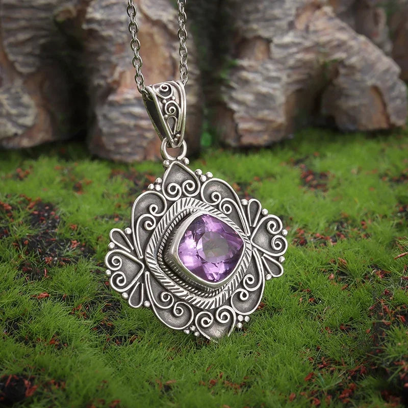 Silver pendant with a purple gemstone on a grassy background
