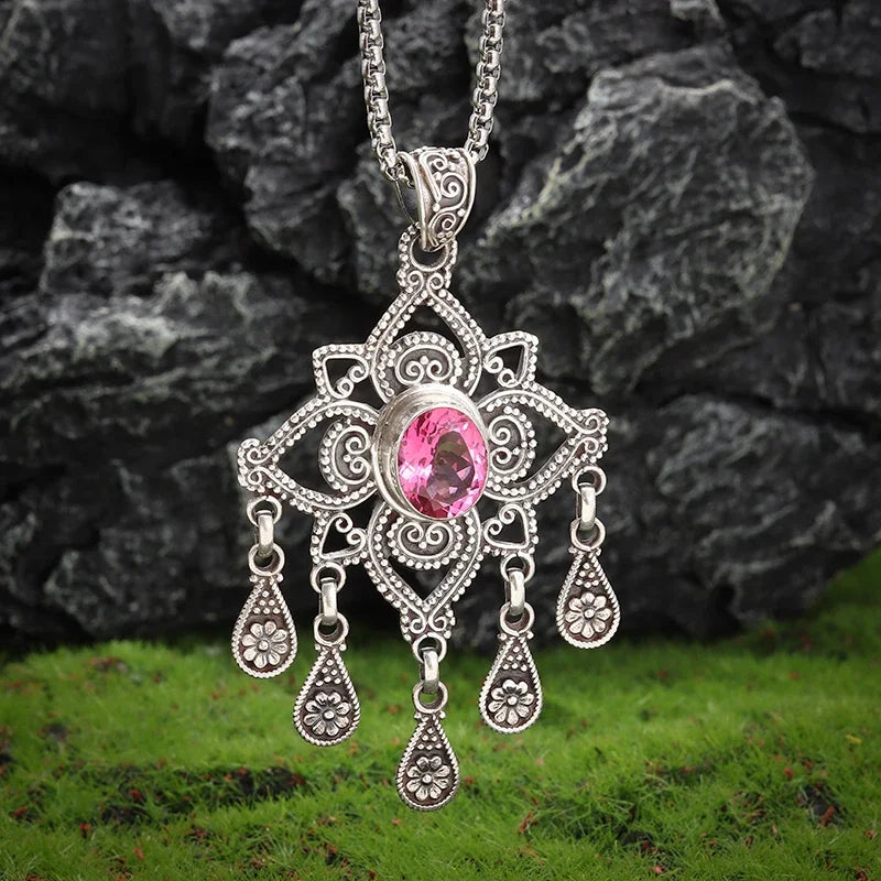 Decorative silver pendant with a pink gemstone on a chain against a natural background.