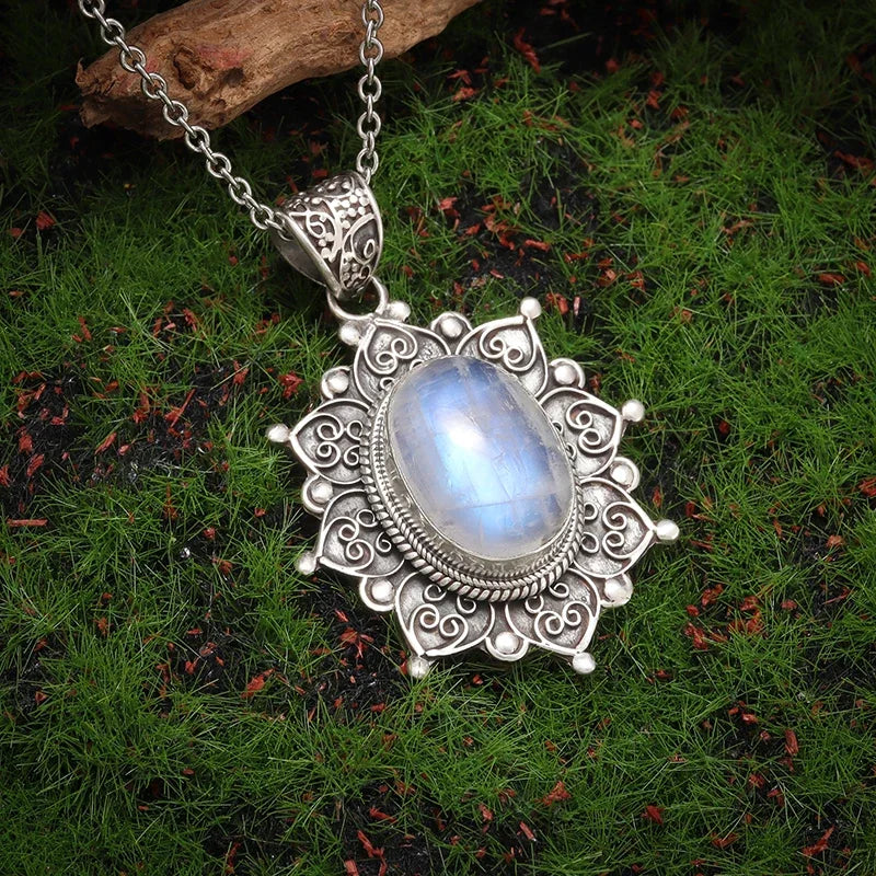 Silver pendant with a blue gemstone on a chain, placed on green grass.