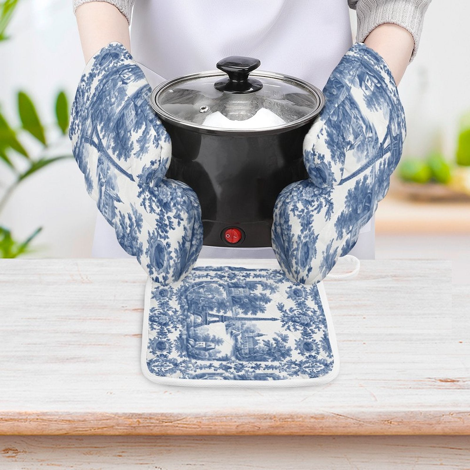 Person wearing blue and white patterned oven mitts holding a small black appliance.