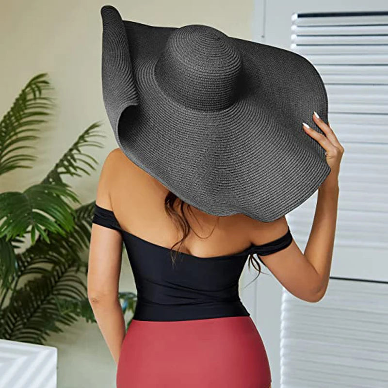 Woman wearing a large black sun hat indoors with a plant in the background