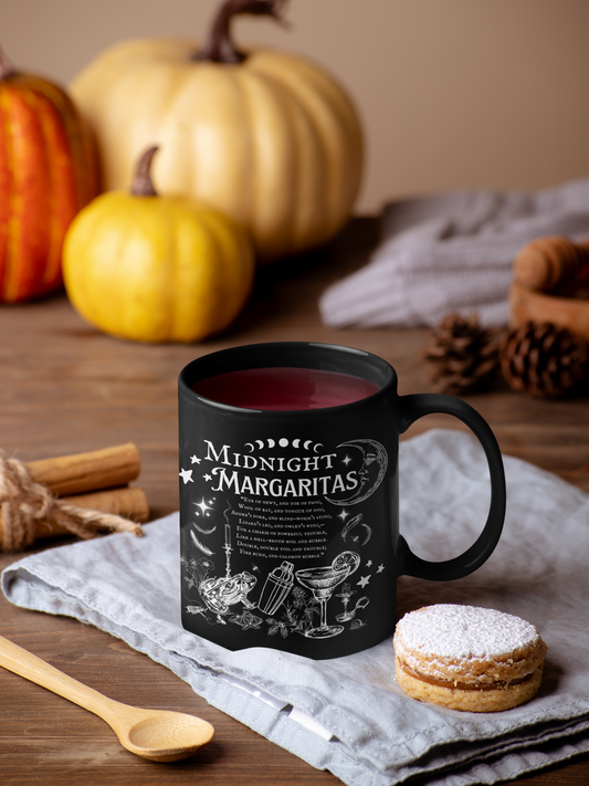 Black mug with 'Midnight Margaritas' text on a wooden table with pumpkins and cookies.