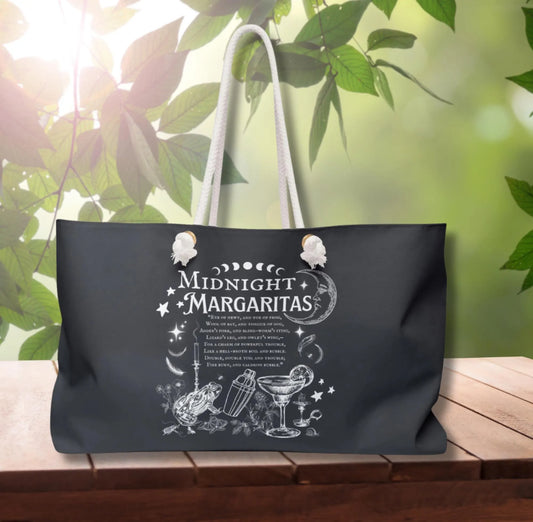 Black tote bag with 'Midnight Margaritas' design on a wooden surface with greenery in the background