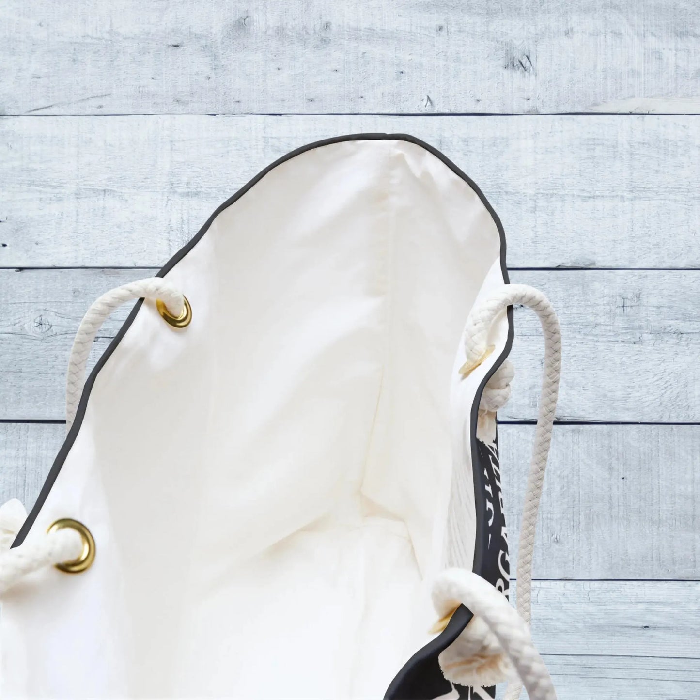 White drawstring bag with gold accents on a light wooden surface