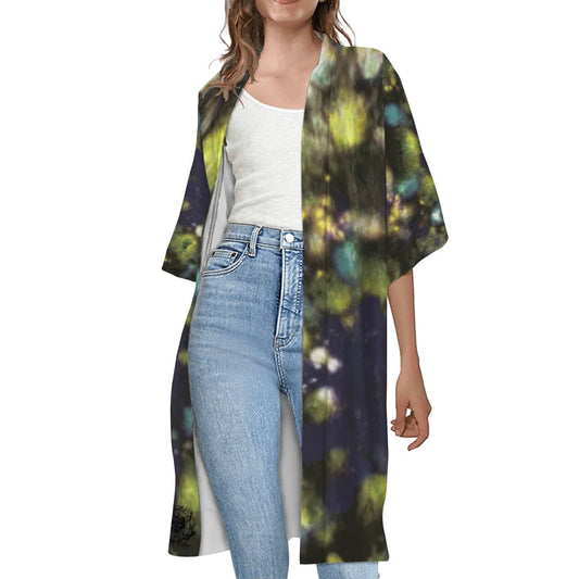 A woman wearing a short sleeve cape with a geometric pattern in multicolor, paired with a white top and blue jeans.