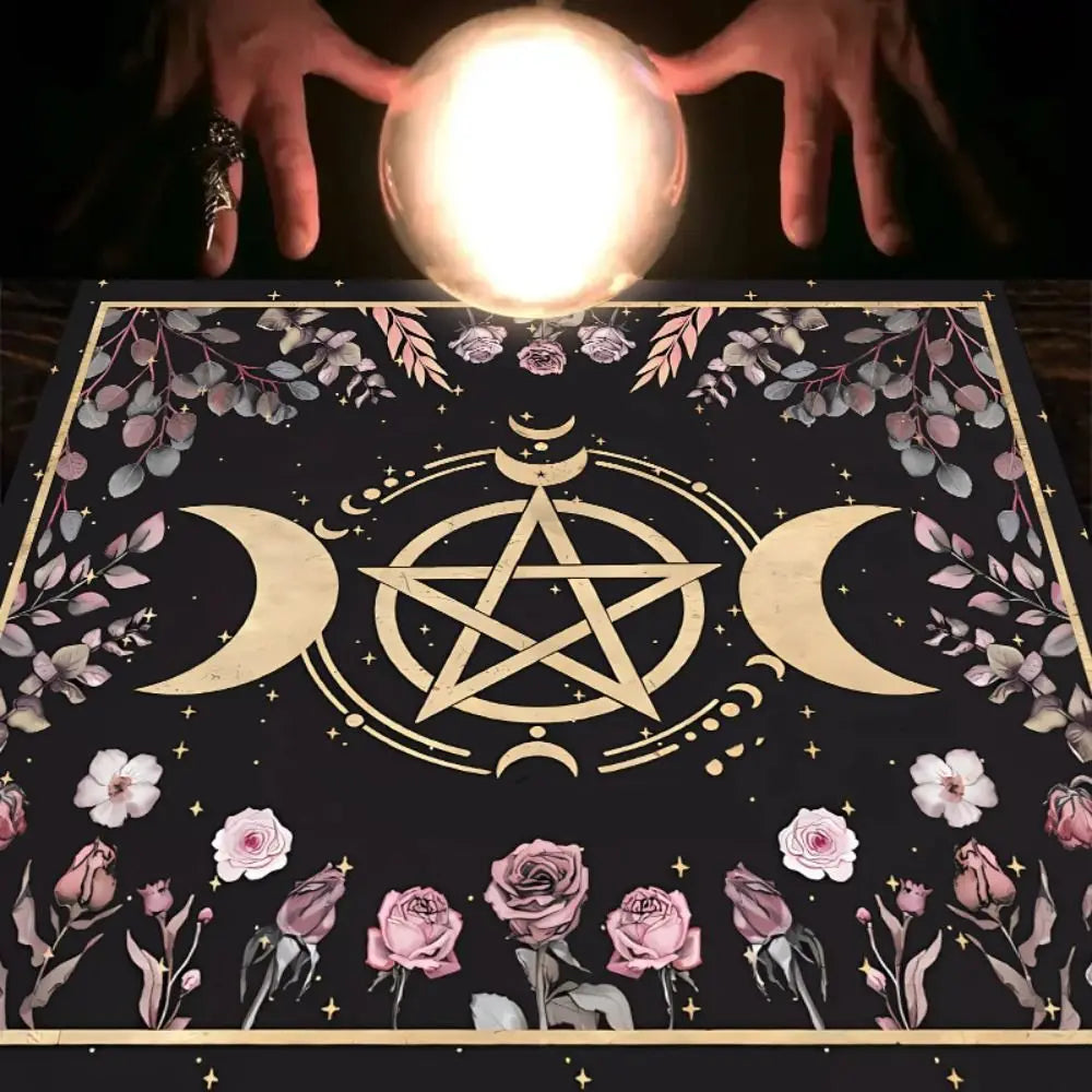 Crystal ball held by hands on a table with a decorative cloth featuring floral and pentagram designs.
