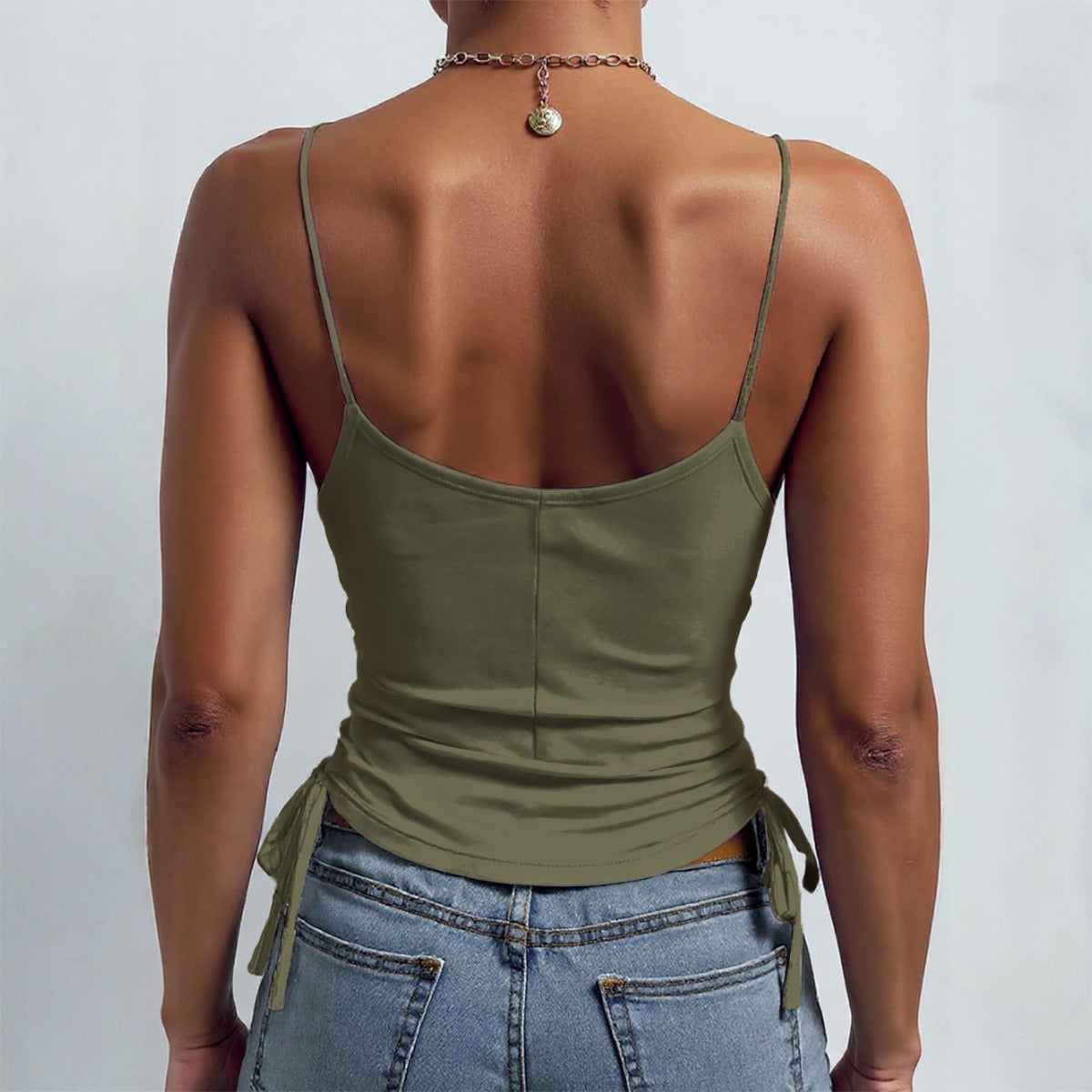 Person wearing an olive green tank top with thin straps and tied sides, paired with blue jeans on a light gray background.