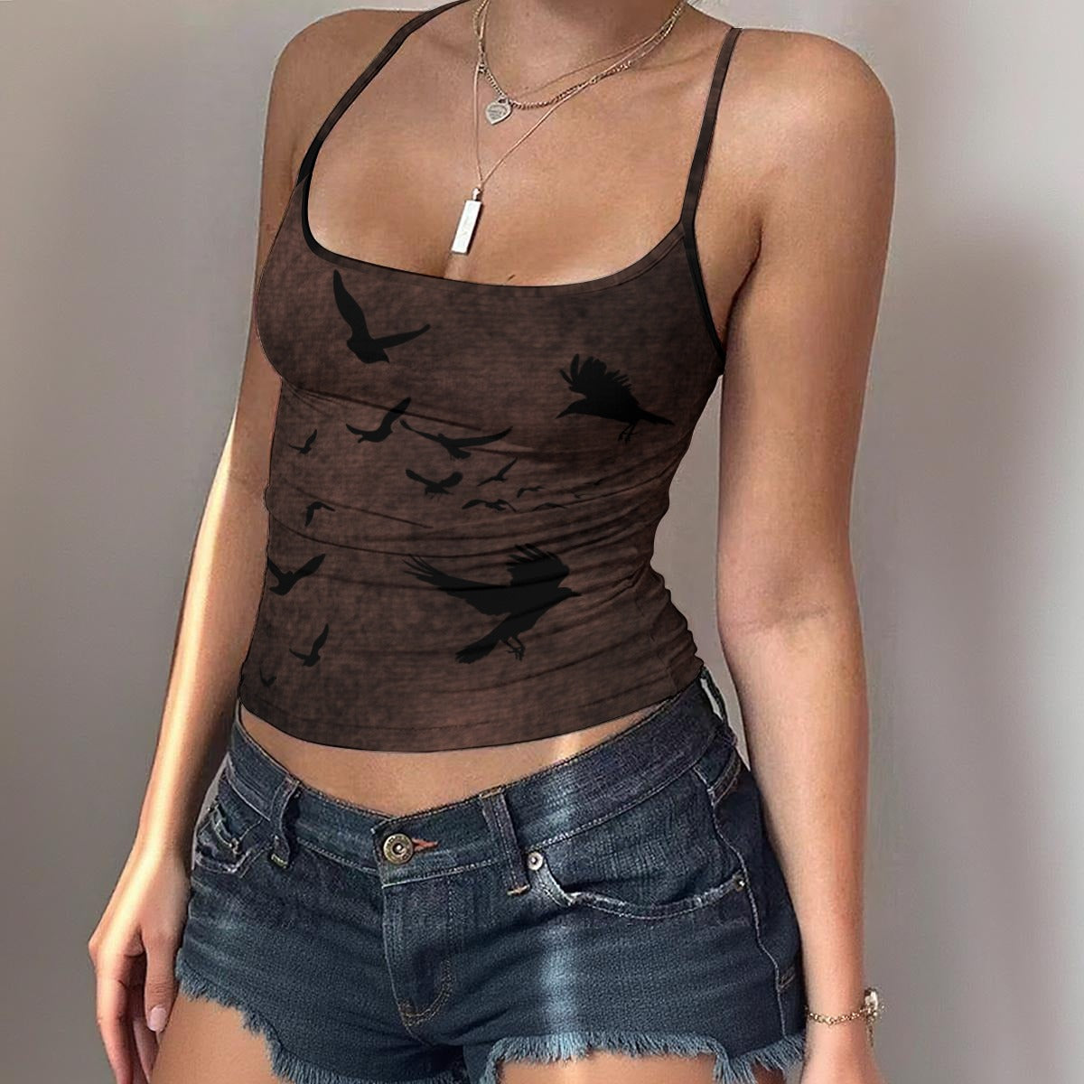 Person wearing a brown tank top with black bird silhouettes and denim shorts against a plain background
