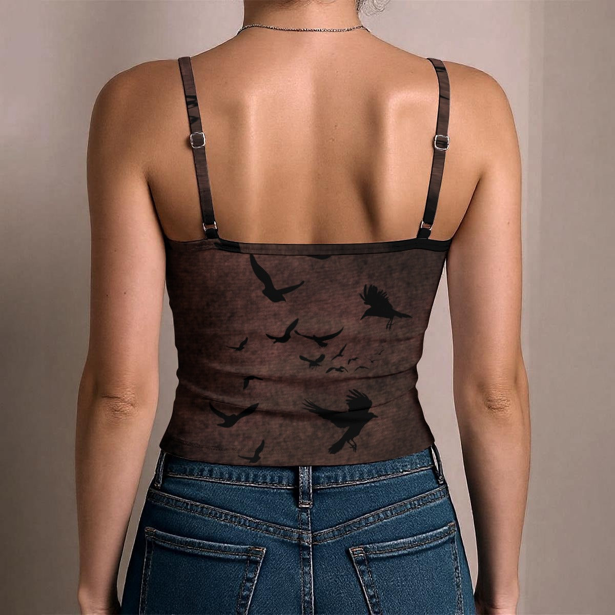 Person wearing a brown tank top with black bird patterns and blue jeans on a beige background