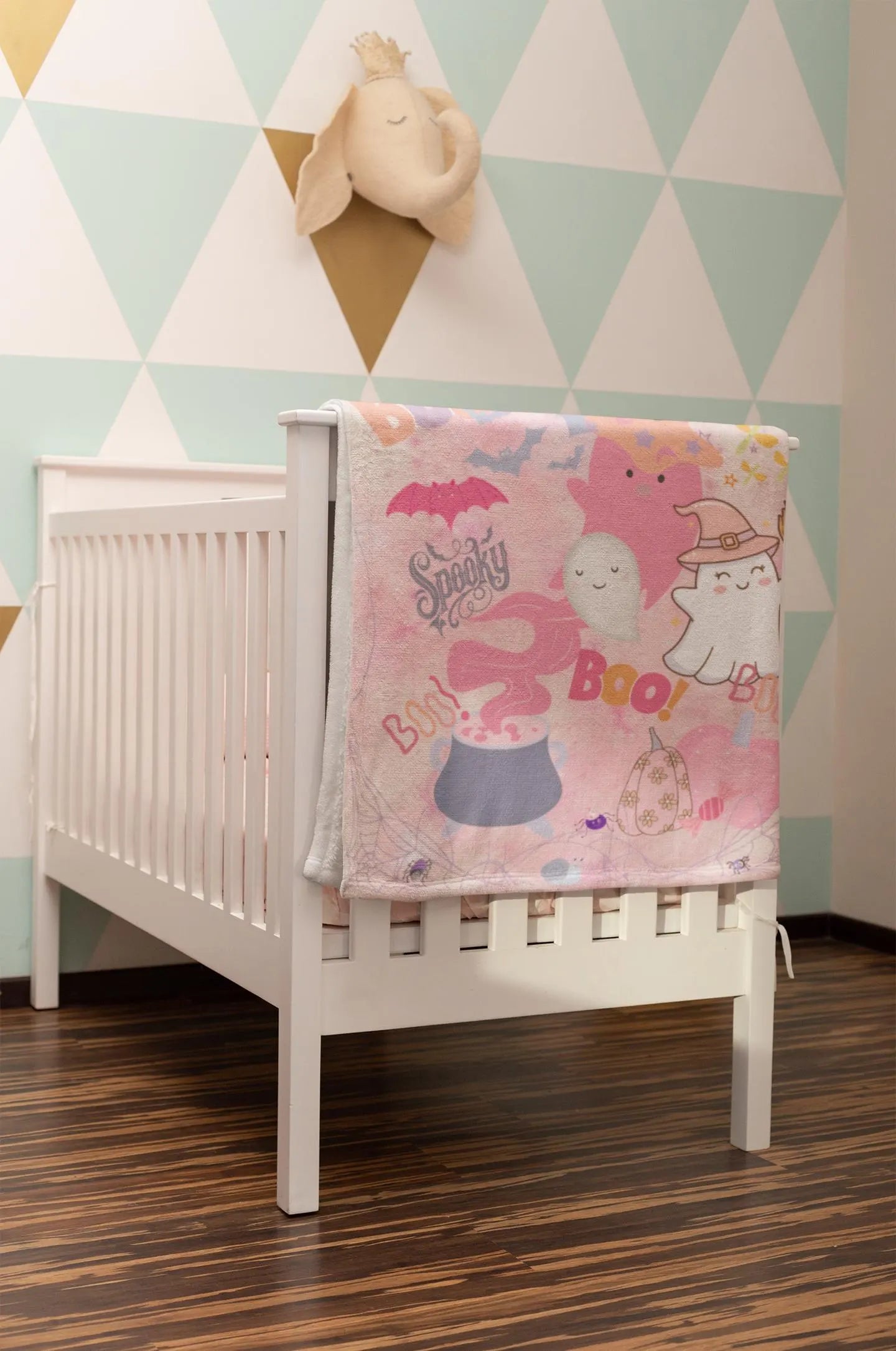 White crib with a pink blanket featuring cartoon characters in a room with geometric wall design.